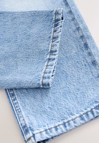 Tessuto di denim azzurro chiaro piegato, che mostra un orlo sfrangiato e una texture sottile con cuciture a contrasto arancioni lungo le cuciture.