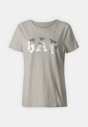 Lys grå bomulls t-skjorte med et stort, metallisk sølvfarget "GAP" logo over brystet. Korte ermer og rund hals.