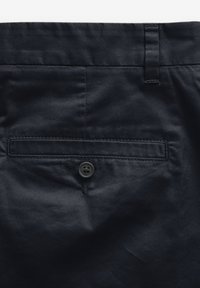 Námořnické modré kalhoty s hladkým povrchem, které mají zadní kapsu s knoflíkovým zapínáním a poutko na pásek.