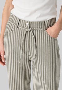 Olive green striped pants with a belted waist, featuring white vertical stripes, side pockets, and a silver button closure.