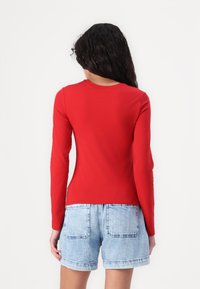 Tricou roșu cu mâneci lungi, guler rotund, textură netedă, design ajustat și tiv curbat, asociat cu pantaloni șort din denim de un albastru deschis.