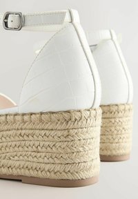 Sandalias de plataforma blancas con parte superior de textura de cocodrilo, correa de tobillo ajustable y suela de cuña trenzada de yute.
