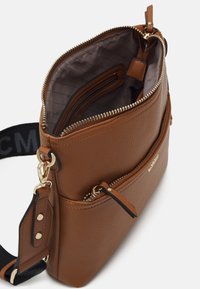 Borsa a tracolla in pelle marrone con cerniere dorate, tasca frontale e tracolla nera regolabile parzialmente visibile su uno sfondo bianco.