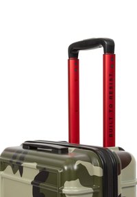 Hardshell kufr v zeleném maskáčovém vzoru, s černým zipem, červenou teleskopickou rukojetí a textem "BUILT TO RESIST" a texturovaným povrchem.