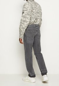 Vaqueros de mezclilla gris con un ajuste relajado, bolsillos traseros y dobladillos enrollados, combinados con una camiseta de manga larga camuflada y zapatillas blancas.