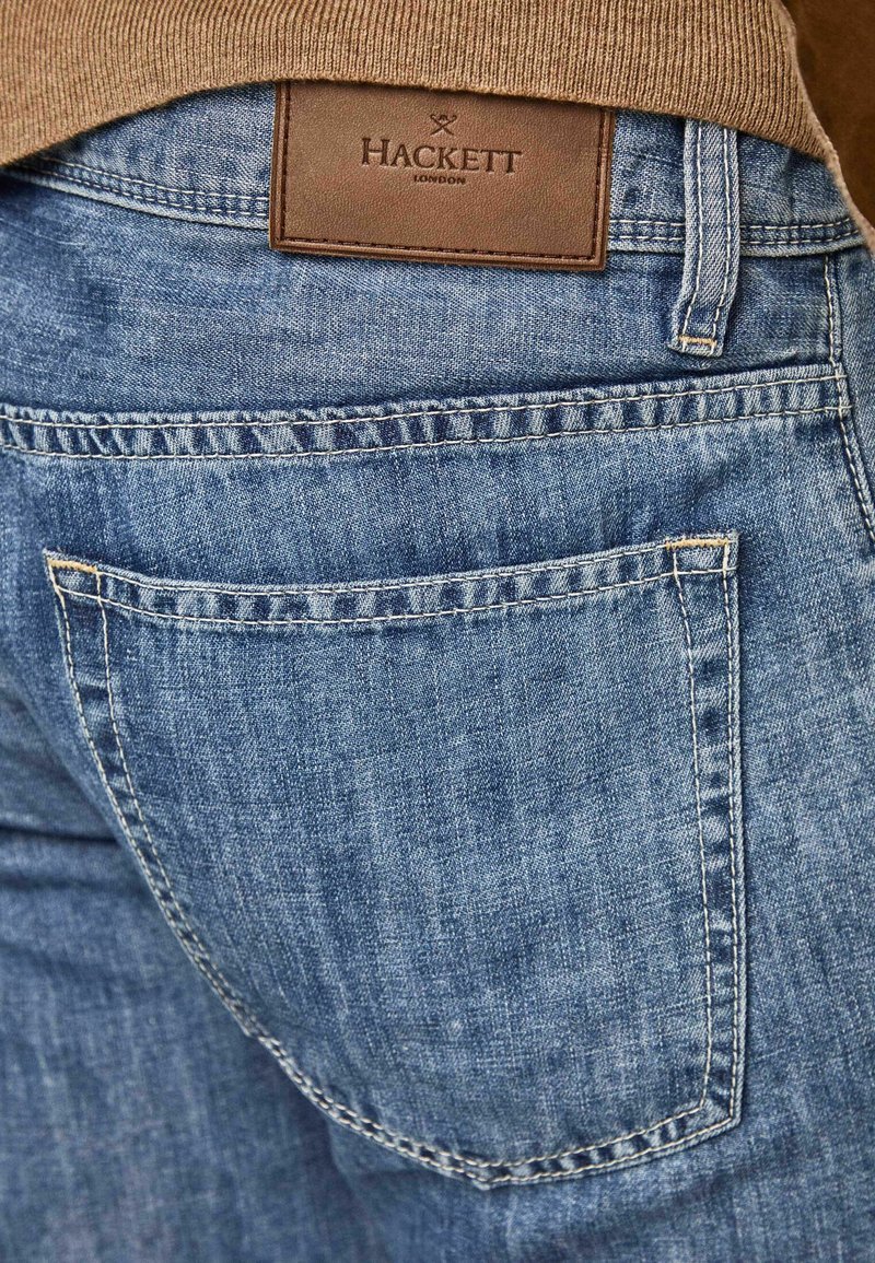 Jeans de mezclilla en azul claro con un acabado texturizado. Presentan una etiqueta de cuero con la inscripción "HACKETT LONDON" en la cintura y un diseño estándar de bolsillos traseros.
