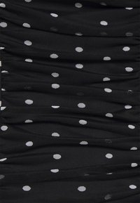 Tissu noir à pois blancs, présentant un design texturé et froncé. Le motif est uniformément réparti sur le matériau.