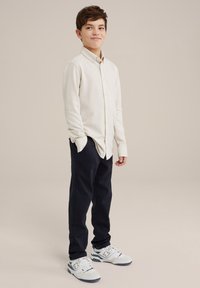 Camisa de manga larga color beige claro, pantalones azul marino y zapatillas blancas. Corte relajado, cuello abotonado y tela texturizada.