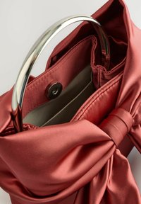 Rdeča torbica iz satena z veliko pentljo in srebrnim okroglim ročajem, z zapenjalom na pritrditev in notranjostjo brez podloge.