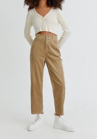 Cardigan crème court côtelé et pantalon en velours côtelé marron clair présentent des rayures verticales, une taille haute et deux poches avant, assortis à des baskets blanches.