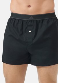 Černé bavlněné boxerky s elastickým pasem, který má šedé logo, funkční přední knoflík a jednoduchou, hladkou strukturu.