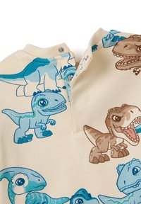 Prenda de algodón en color crema con estampados de dinosaurios de dibujos animados en azul y marrón. Cuenta con un cierre a presión en el cuello y un cuello acanalado.