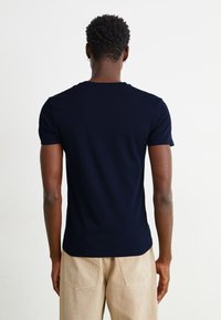 Tricou bleu marin cu mânecă scurtă, design ajustat, din material de bumbac. Textură netedă cu un guler discret, prezentat din spate.