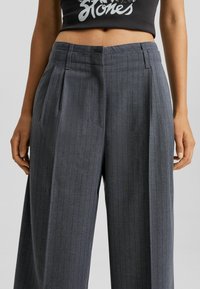 Grå rutiga byxor med skräddarsydd passform, veckad front, bälteshällor och sidofickor, tillverkade av ett mjukt tyg.