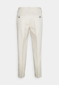 Pantalon beige clair à texture lisse, avec deux poches arrière, des boutons noirs et une coupe fuselée.