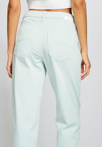 Světlé zelené kalhoty s vysokým pasem a volným střihem. Mají zadní kapsy a čistý pas s visačkou. Hladká, mírně strukturovaná tkanina.