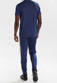 Marinhållen träningsoutfit med en kortärmad topp och avsmalnande byxor. Byxorna har kontrasterande sidosträck och en figurnära design.