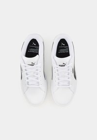 Scarpe da ginnastica bianche con una tomaia in pelle liscia, chiusura con lacci, una striscia nera di accento e un logo sul lato e sulla soletta.