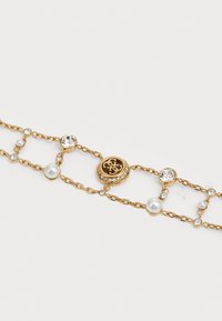 Gouden armband met afwisselend parel- en kristalaccenten, versierd met een decoratief circulair embleem, verbonden door een fijn kettingontwerp.