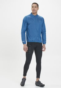 Lätt blå jacka med full dragkedja och ståkrage, tillsammans med svarta tajta leggings med texturerade detaljer och svarta träningsskor.