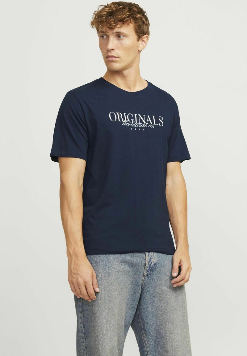 Granatowa bawełniana koszulka z okrągłym dekoltem, z białym nadrukiem "ORIGINALS Worldwide Co. 1990" na piersi. Krótkie rękawy.