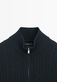 Maglione in cotone blu scuro con zip, collo alto a coste e trama a trecce. Include una zip argentata e un'etichetta del marchio all'interno.