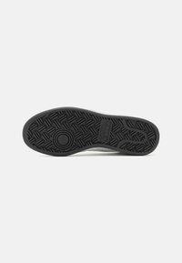 Shoe sole featuring a textured black rubber material with circular and zigzag patterns for grip and traction, designed for durability.