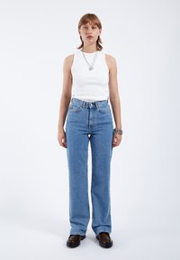 Vit ribbad linne med hög hals, kombinerat med högmidjade, ljusblå jeans och svarta platåskor. Lager av silverhalsband.