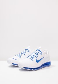 Vita sportskor med blå detaljer, överdel i mesh och luftdämpning i sulan. Har blå snörningar och Nike-logotyp på sidan.