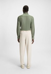 Groene langemouwshirt met een rechte zoom, gecombineerd met crèmekleurige, losse broek met elastische tailleband en zijzakken.
