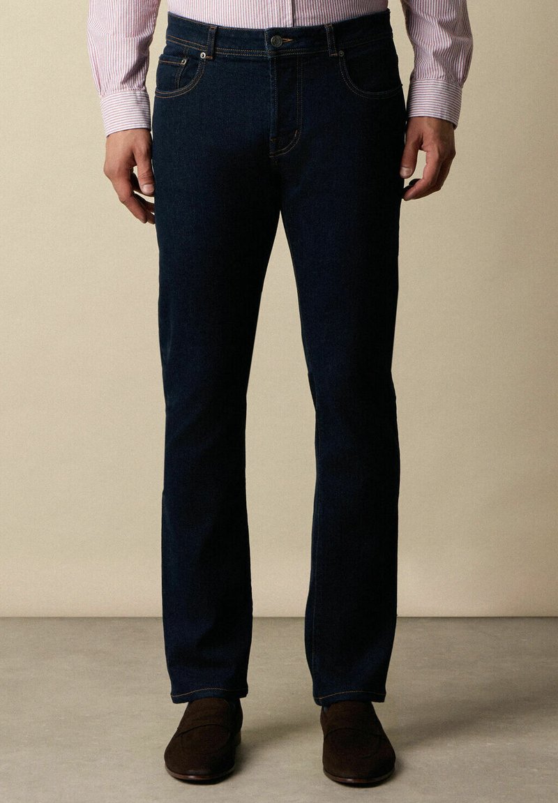 Jeans in denim blu scuro a gamba dritta, con chiusura a bottone e cerniera, cinque tasche e dettagli di cucitura in contrasto.