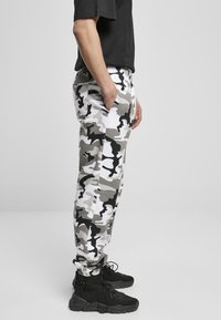 Szürke, fehér és fekete terepminta joggers. Rugalmas derék, zsebekkel. Fekete magas szárú sneakers-szel párosítva. Sima szövet és slim fit.
