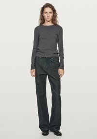 Szary top z długim rękawem w połączeniu z ciemnoniebieskimi dżinsami. Dopasowany fason topu kontrastuje z szerokimi spodniami. Oba elementy mają prosty design.