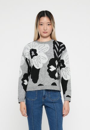 Grå strikkegenser med blomsterdesign i svart og hvitt, rund hals, og ribbede ermer. Kombinert med blå denim høytlivsjeans.