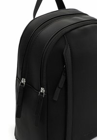 Czarny plecak z tkaniny z dwoma zamykanymi na zamek komorami, płaskimi paskami i srebrnymi elementami. Gładka tekstura z minimalistycznym wzornictwem.