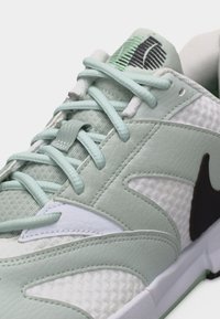 Zbliżenie na jasnozielony i biały sneaker marki Nike z fakturowaną skórą, siateczkową tkaniną oraz czarnym logo Swoosh po boku.