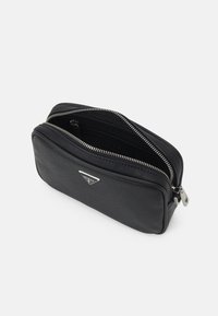 Schwarze Lederhandtasche mit strukturierter Oberfläche, zwei Reißverschlussfächern und einem silbernen Logo-Detail auf der Vorderseite. Kompakte, rechteckige Form.