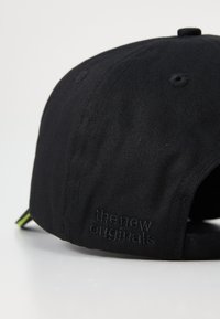 Svart baseballcap med brodert logo bak, laget av teksturert stoff. Har en buet skygge og justerbar stropp bak.