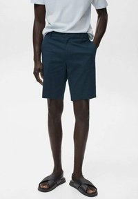 Navy blue shorts in a relaxed fit, made of lightweight fabric, featuring a flat front and side pockets. Paired with black sandals.