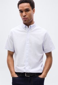 Πουκάμισο με κοντά μανίκια σε ανοιχτό μωβ χρώμα, κατασκευασμένο από βαμβάκι, με γιακά και εμπρόσθιο ντεκολτέ με λευκά κουμπιά. Φοράται με σκούρο τζιν.