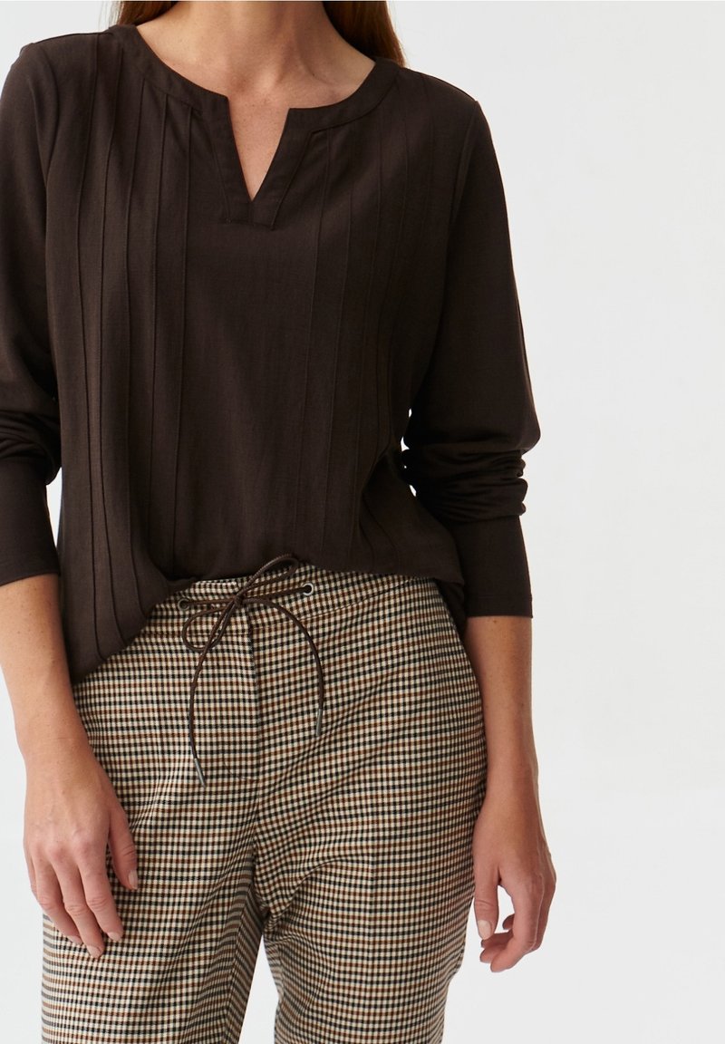 Haut marron foncé à plis verticaux et col en V, associé à un pantalon à carreaux avec une taille à cordon de serrage et des tons neutres.