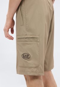 Μπεζ σορτς από ελαφρύ ύφασμα, με πλαϊνή τσέπη, πίσω τσέπη και κεντημένο λογότυπο EA7 στο πόδι.