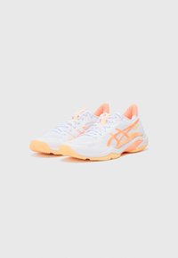 Baskets de sport blanches avec des accents orange clair. Tige en maille pour la respirabilité, semelle extérieure en caoutchouc texturé et design de semelle intermédiaire rembourrée.