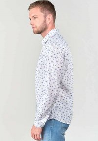 Wit overhemd met lange mouwen en een klein paars bloemenpatroon, met een geknoopte kraag en een slim-fit pasvorm, gecombineerd met lichtblauwe denim jeans.