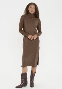 Barna garbó ruha puha kötött anyagból, hosszú ujjakkal, oldalsó hasítékokkal és térd fölé érő hosszúsággal, sötétbarna cowboy csizmákkal párosítva.