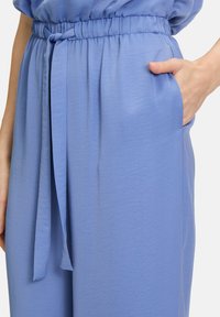 Pantalons en tissu texturé bleu clair avec taille élastique et détail à nouer, dotés de poches latérales pour plus de fonctionnalité.
