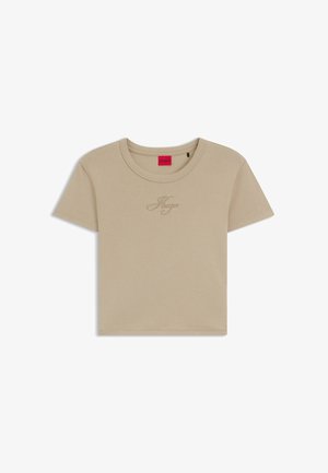 T-shirt court beige à manches courtes, col rond, avec un logo "Hugo" brodé discret sur la poitrine, étiquette intérieure rouge.