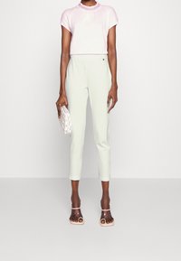 Jasnoróżowy krótki top z rękawami i zdobieniem z koralików na dekolcie, w połączeniu z jasnopistacjowymi dopasowanymi spodniami. Dodatki w jasnych kolorach oraz przezroczyste sandały na obcasie.