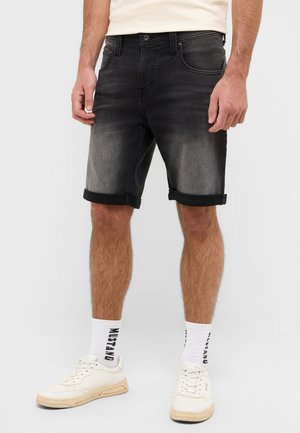 Schwarze Jeansshorts mit Verblassungen, umgeschlagenen Saum, fünf Taschen und einem Knopfverschluss. Gestylt mit weißen Sneakers und Crew-Socken.