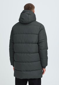 Mørkegrøn polstret pufferjakke med hætte, der har vandret syninger, elastiske manchetter og en mellemlang design.